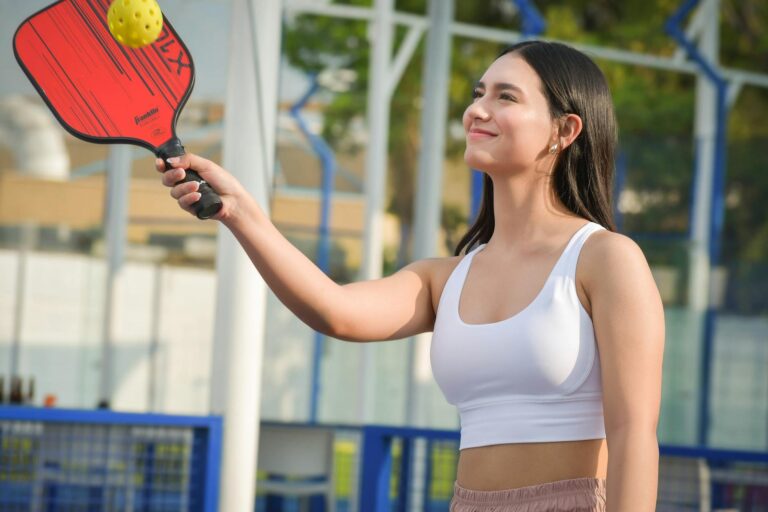 Young woman playing pickleball outdoors wearing sportswear, enjoying a sunny day.