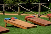 Wooden cornhole boards with colorful bean bags on a green lawn during a sunny day outdoors.