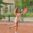 Energetic young female tennis player swings racket on outdoor clay court.